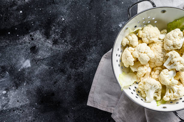 istock Fresh white heads cleaned cauliflower in a colander. Black background. Top view. Copy space 1211804976