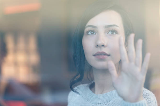 istock Beautiful Young Woman looking through the window 1211807158