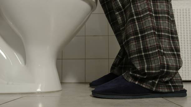 el primer plano de las piernas masculinas en pijama y zapatillas llega a un baño - orina fotografías e imágenes de stock