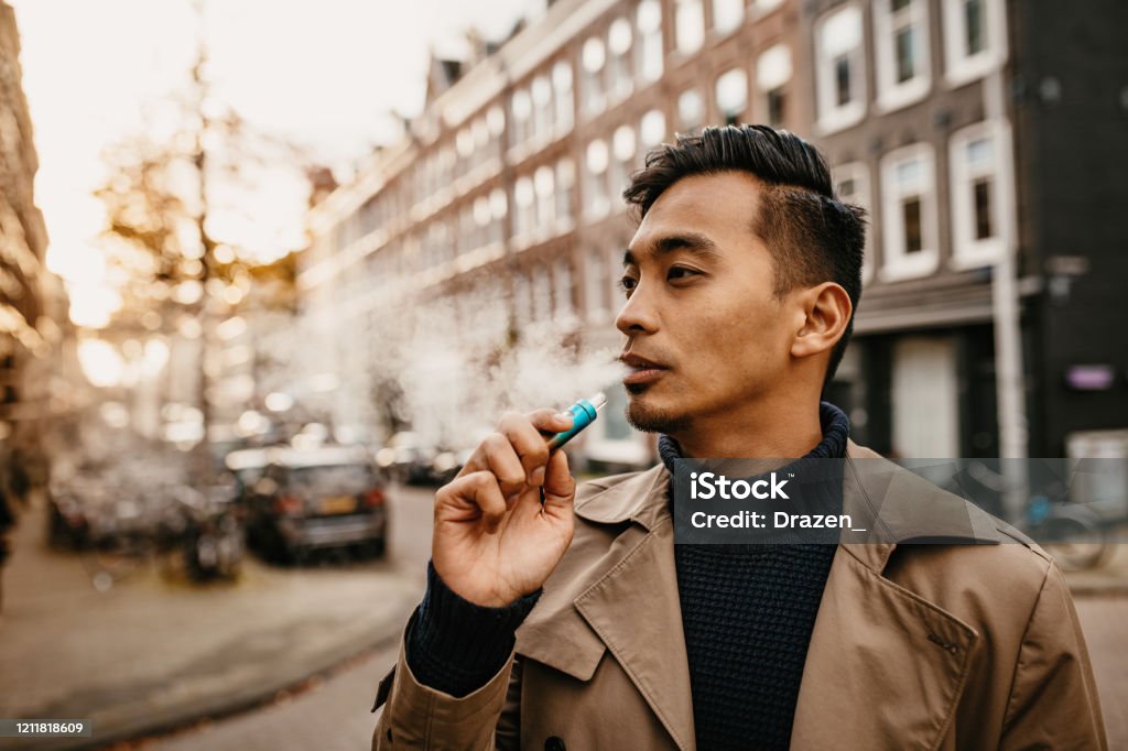 Japanese man vaping in the street Smoking electronic cigarette in the city outdoors Electronic Cigarette Stock Photo