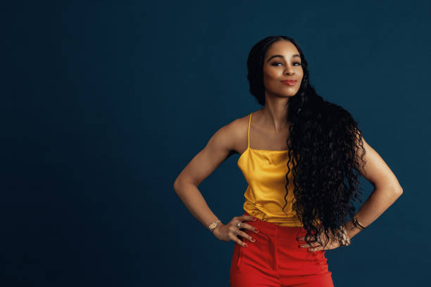 Portrait of a confident young woman with very long  beautiful black curly hair smiling with arms on waist Portrait of a confident young woman with very long  beautiful black curly hair smiling with arms on waist black woman hair extensions stock pictures, royalty-free photos & images