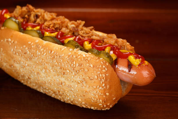 Danish hot dog with pickled cucumbers, fried onions, ketchup and mustard. On a wooden table. Close-up. stock photo