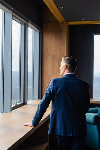 istock back view of businessman in suit looking through window 1211821946
