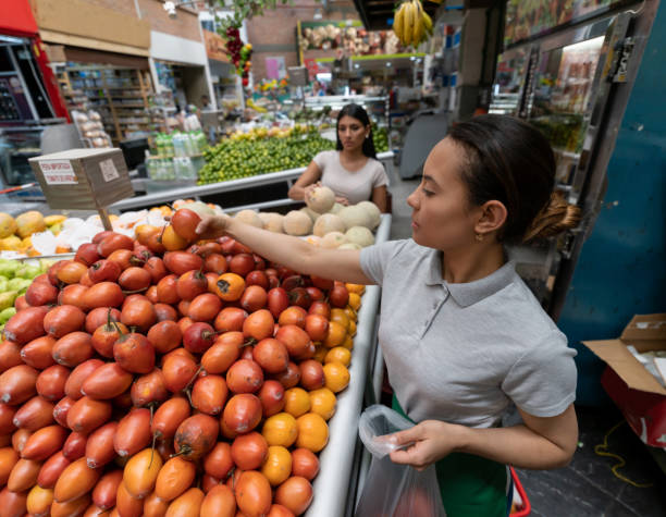 istock Latin american vendor helping female customer choose tomato fruit and adding them into a plastic bag 1211822053