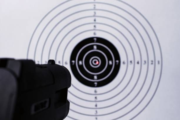 istock Background with a pistol aimed at a round target with a red dot from a laser sight in the center. Business Goal Achievement Concept 1211826073