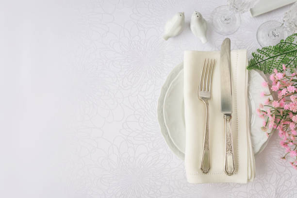Classic serving for a gala dinner with luxurious porcelain, silverware and spring flowers on a white tablecloth, with copy-space, top view