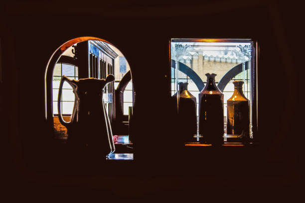 stilllife-ansicht von fenstern durch cubbies mit geätztem glas in einer dunklen kneipe mit tischen und einem schloss, das durch ferne fenster betrachtet wird - etched glass windows stock-fotos und bilder