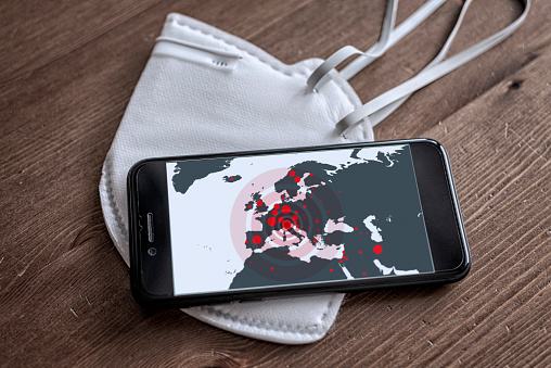 Coronavirus (2019-nCoV) is spreading all over the Europe, mobile phone with map and alerts spots is lying on the white face mask.