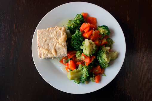 steamed broccoli and carrots with chicken soufflé and sauce on a white plate