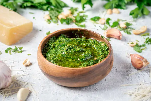 Homemade pesto sauce in a wooden bowl and ingredients for cooking on a gray background close-up. Italian food.