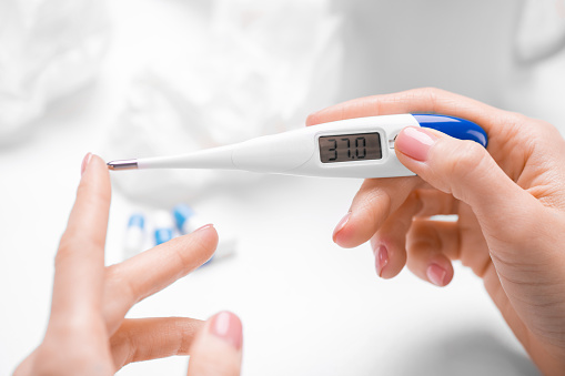 Close-up of unrecognizable woman checking body temperature on digital thermometer at table