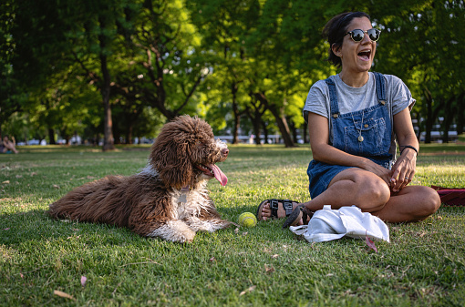 Carefree adult woman, relaxing at public park in Buenos Aires while playing with her dog on a sunny day