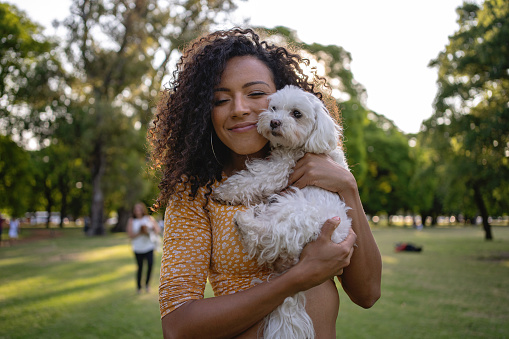 Carefree young woman, relaxing at public park in Buenos Aires while holding her dog bichon frise
