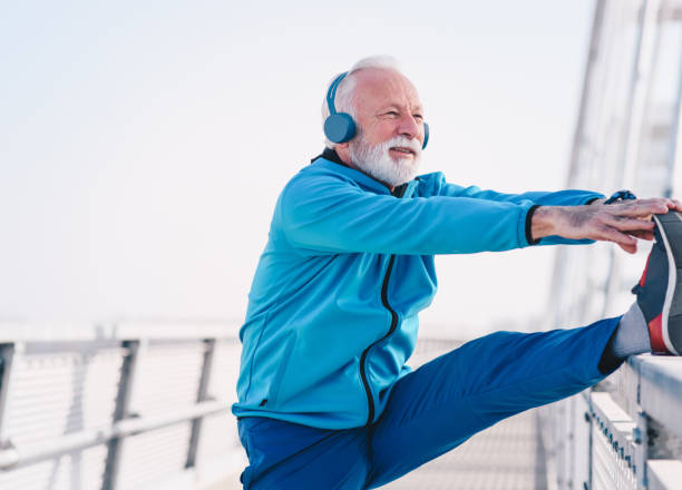 istock A senior sportsperson stretching his legs on a bridge walkway. He is stretching by pulling toes of a leg raised on a walk rail. He is wearing headphones. 1211835292