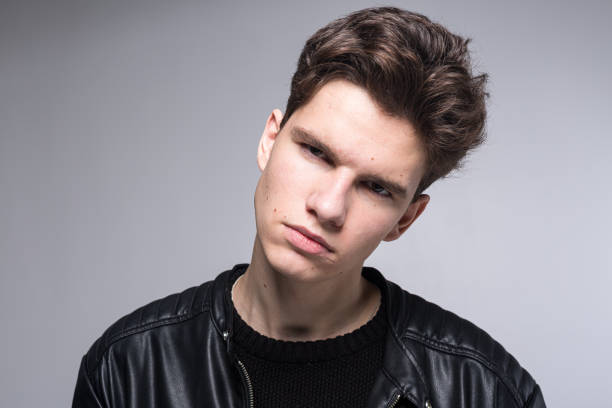 Wide angle. Studio shot. Young caucasian guy model in black clothes posing in the studio. Teenager in Leather Jacket Standing Against White Background. young fashion model wearing black coat in studio