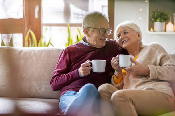 elderly couple drinking coffee together on the sofa at home - coffee at home imagens e fotografias de stock