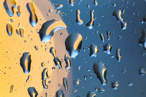 Macro serum drop with bubbles on the colored water. Selective focus of a moving drop with smooth multicolor background (blue, yellow, white and magenta).