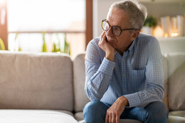 zmartwiony starszy mężczyzna siedzący samotnie w swoim domu - worried sadness men senior adult zdjęcia i obrazy z banku zdjęć