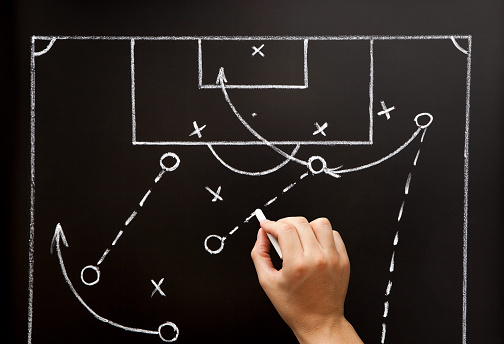 Football soccer coach drawing game playbook, tactics and strategy with chalk on blackboard.