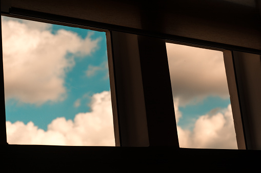 Square windows that shows a clear blue sky at the outside, during a sunny day with white clouds.