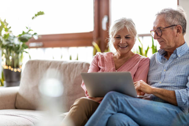 mature couple using a laptop while relaxing at home - comfortable relaxation sofa men imagens e fotografias de stock