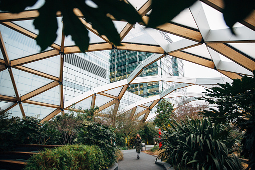Woman in winter coat walking in hidden location at Canary Wharf, roof garden at Crossrail Place, London, UK
