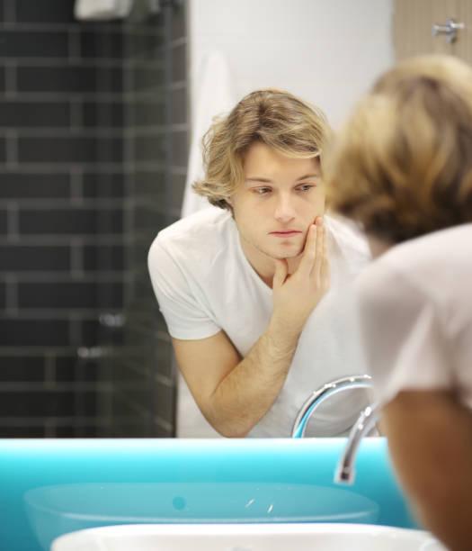 istock young man looking in the mirror,combing his hair,looking at problems on face 1211859908