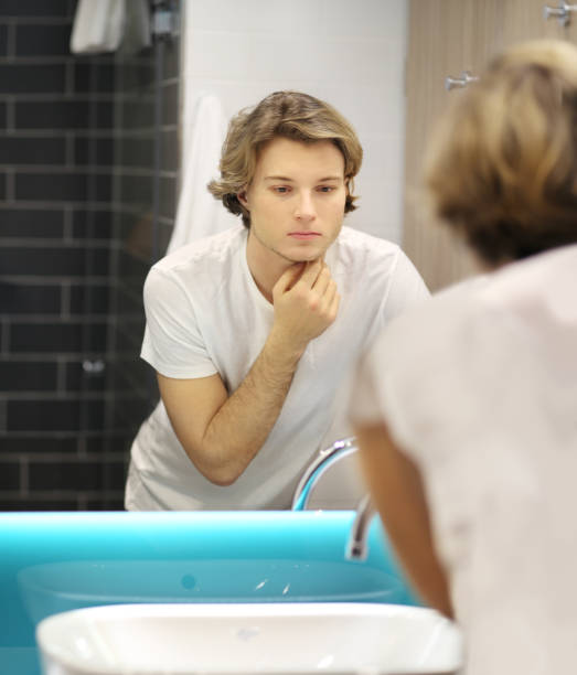 istock young man looking in the mirror,combing his hair,looking at problems on face 1211859910