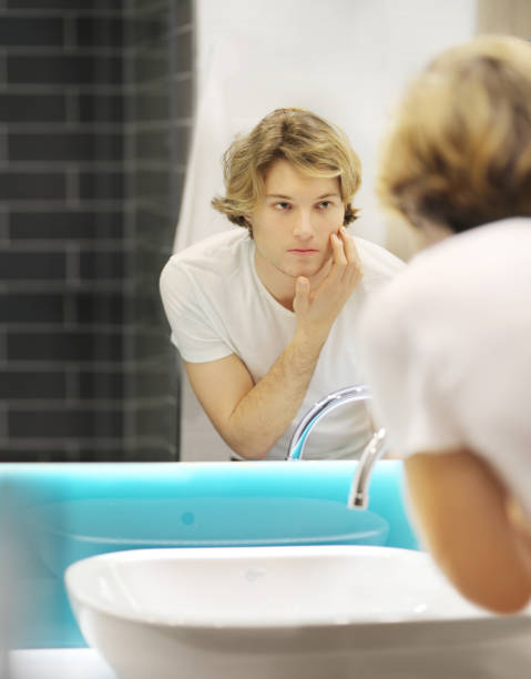 istock young man looking in the mirror,combing his hair,looking at problems on face 1211859911
