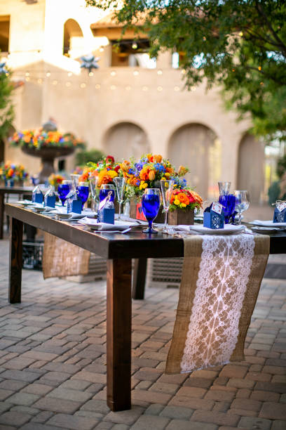 istock Table setting for a wedding celebration in an outdoor mission style patio with blue and orange theme, and flower decorations 1211860187