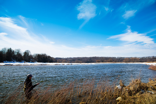 A fisherman stands in a river fishing for rainbow trout on a late winter day.