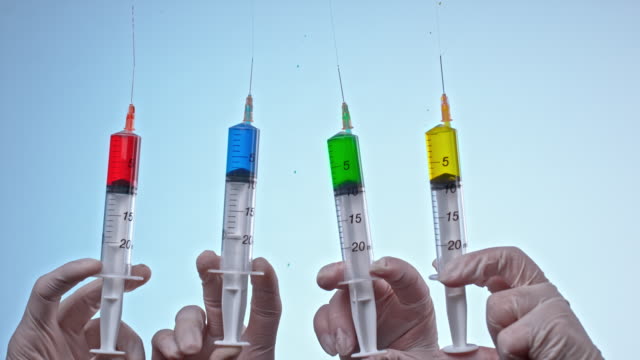 SLO MO LD Four syringes being pressed and red, blue, green and yellow liquid coming out of the needles