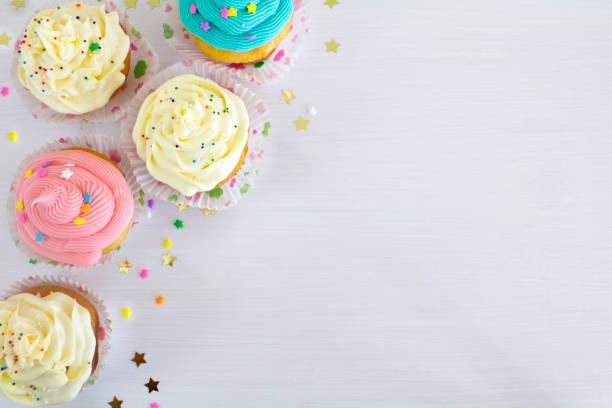 Cupcake background Vanilla buttercream cupcakes with sprinkles, on a white wooden table. dessert topping photos stock pictures, royalty-free photos & images