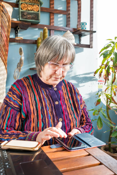 istock Senior Woman Using Phone While Relaxing on Balcony on Sunny Winter Day 1211873436