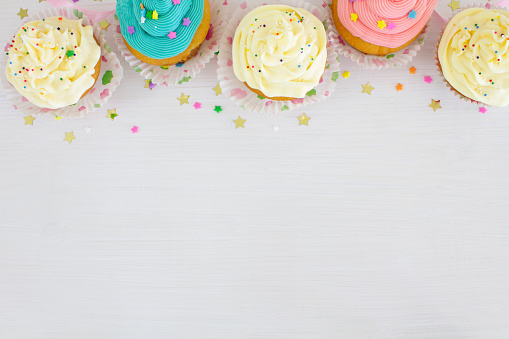 Vanilla buttercream cupcakes with sprinkles, on a white wooden table.