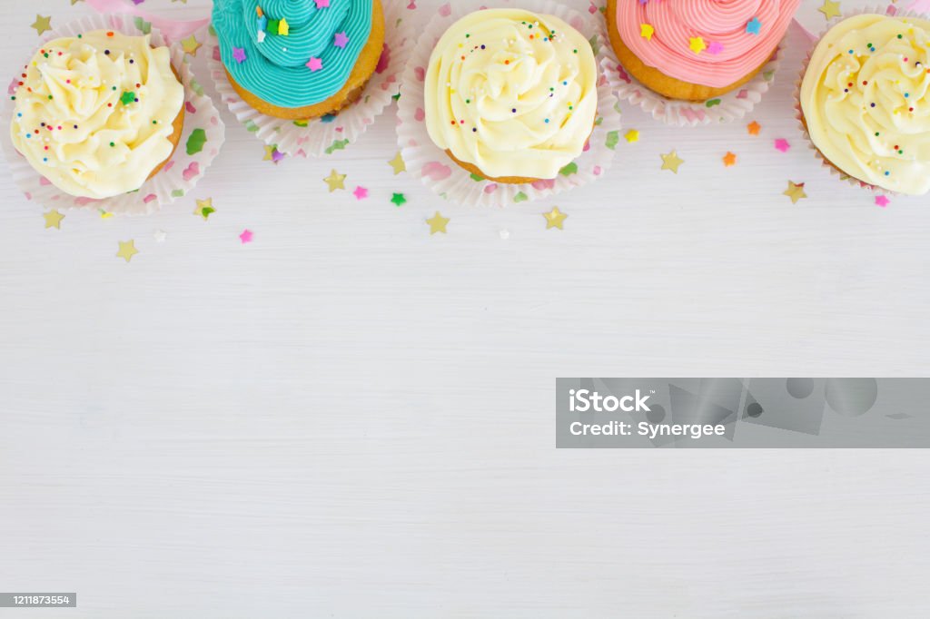 Cupcake Border Vanilla buttercream cupcakes with sprinkles, on a white wooden table. Birthday Stock Photo