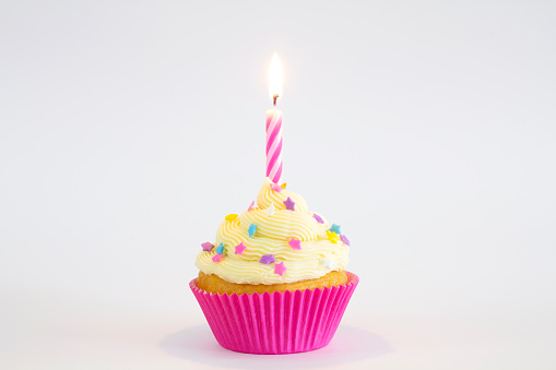 A vanilla and buttercream cupcake with sprinkles, and a lit birthday candle.