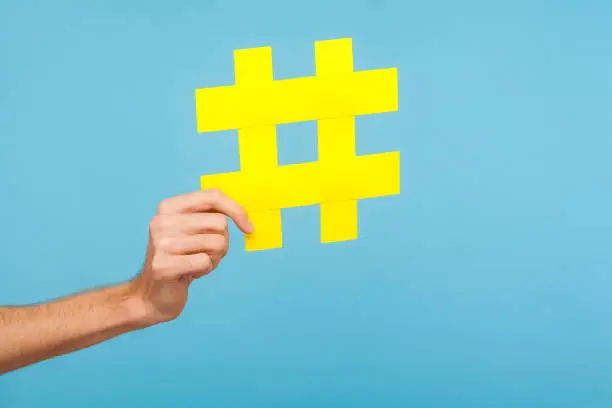 Photo of Closeup of male hand holding big yellow hash sign, hashtag symbol of internet trends and popular blogs