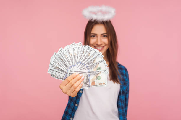 ritratto di allegra donna angelica, vincitrice della lotteria con nimbus sopra la testa che mostra soldi, tenendo banconote in dollari - fondo raggera foto e immagini stock