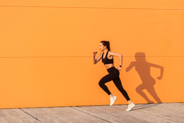 zmotywowana pewna siebie zawodniczka w obcisłej odzieży sportowej, czarnych spodniach i topie, zaczyna bieganie, jogging na świeżym powietrzu - jumping women running vitality zdjęcia i obrazy z banku zdjęć
