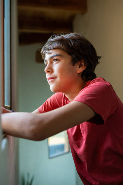 istock latinx preadolescent boy looking through window hopefully, reflecting 1211878525