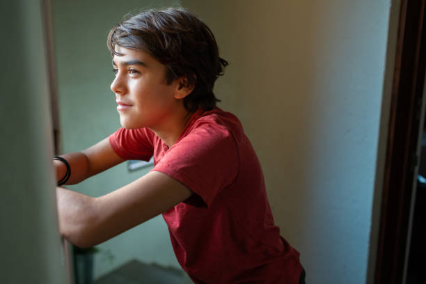 istock hopeful latinx preadolescent boy looking out through window, reflecting, 1211879030