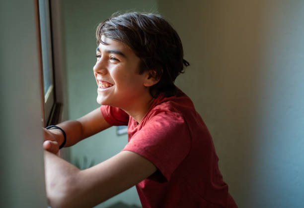 istock latinx preadolescent boy looking out through window cheerfully 1211879071