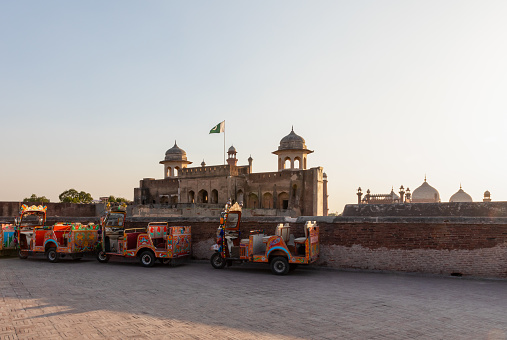 Colorful auto rickshaws (also known as tuk-tuks) outside the Lahore Fort at sunset, Lahore, Punjab, Pakistan. Background is iconic Alamgiri Gate and Badshahi Mosque.