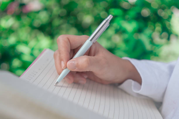 istock Woman hand writing down in small white memo notebook for take a note not to forget or to do list plan for future. 1211886664