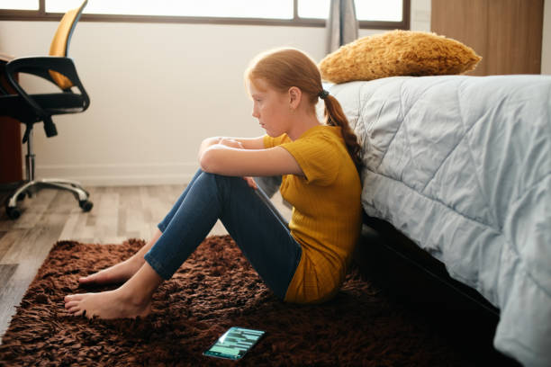 Preteen Bullied Girl Feeling Lonely And Sad At Home Little girl feeling depressed after reading text message on mobile telephone in home bedroom. Concept of bullying and loneliness among preteens preadolescents stock pictures, royalty-free photos & images