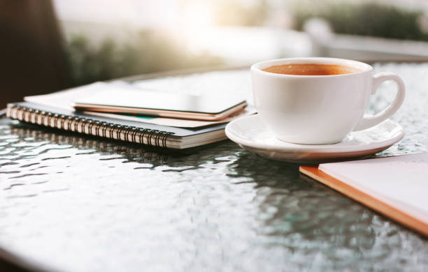 Coffee mug next to notepad and  pencil against afternoon light on wooden table , hammock  garden background. Coffee free time.