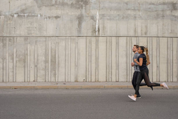мужчина и женщина, бегущие в городе - road running стоковые фото и изображения