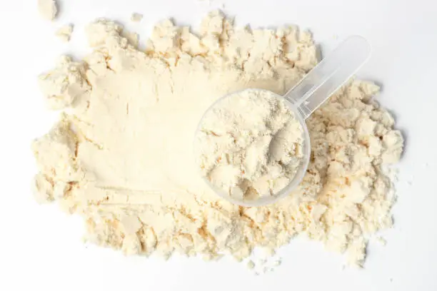 Scattered protein and measuring spoon on a white background top view, concert of sports nutrition.