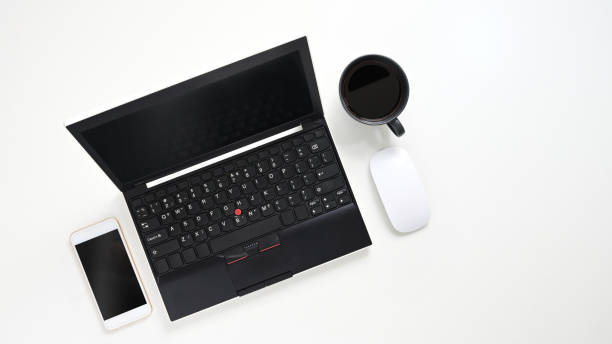 istock Top view image of Black computer laptop putting on white table with coffee cup, cropped white smartphone and wireless mouse. Flat lay office gadgets. Orderly work-space concept. 1211921929